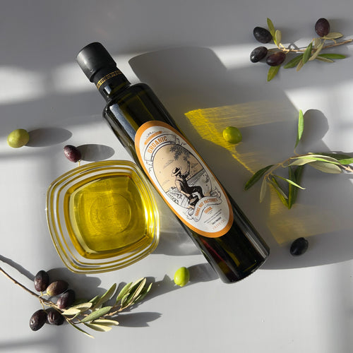 Bottle of olive oil with a label, surrounded by olives on a light background